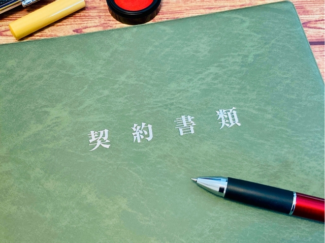 木目の机の上に置かれた契約書類とボールペン、印鑑のイメージ画像